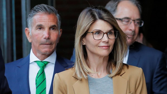 En premier plan, une femme portant des lunettes rectangulaires sourit. En arrière, un homme au regard sérieux la suit.