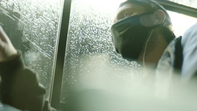 Le rappeur loud porte un masque et est assis dans un bus.