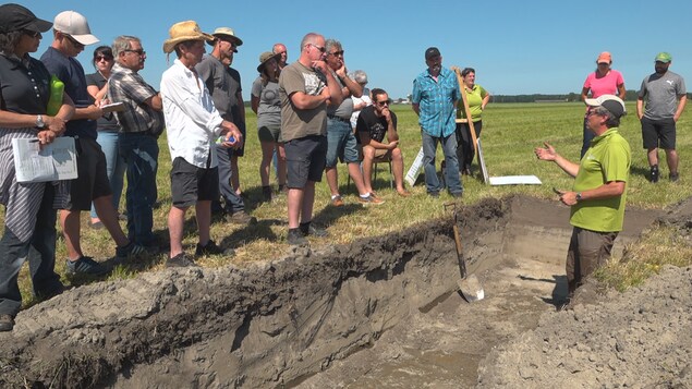 On voit M. Robert dans un trou creusé dans le champ. Il s'adresse au groupe qui se tient près du trou. On voit M. Robert dans un trou creusé dans le champ. Il s'adresse au groupe qui se tient près du trou.