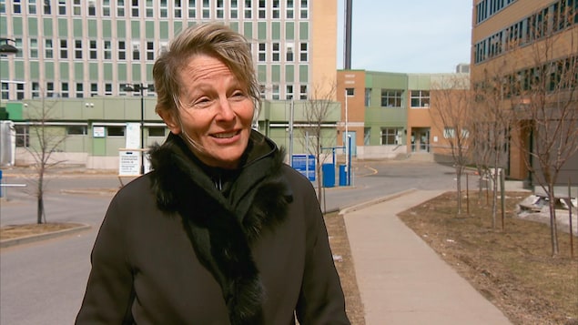 La médecin Louise Caron devant l'hôpital Jeffery Hale à Québec, elle porte un manteau noir. Elle est souriante.
