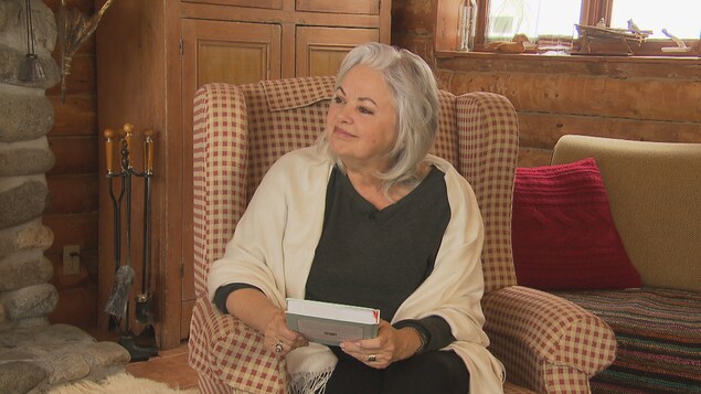 Louise Portal est assise dans un fauteuil et elle tient un livre.