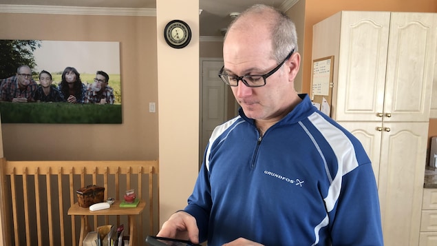 Luc Lawrence, chez lui, regarde son téléphone.