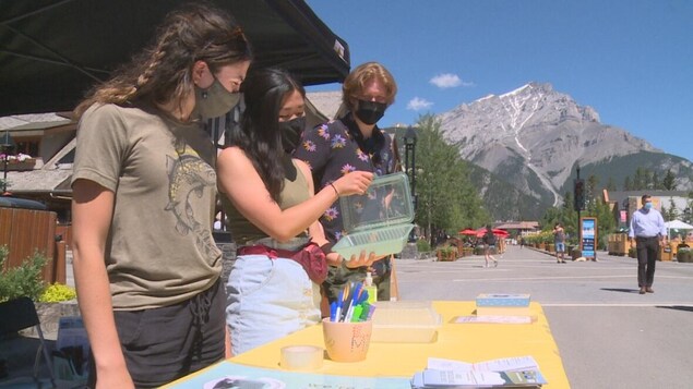 Trois personnes devant une table, la personne du centre tient un contenant réutilisable.