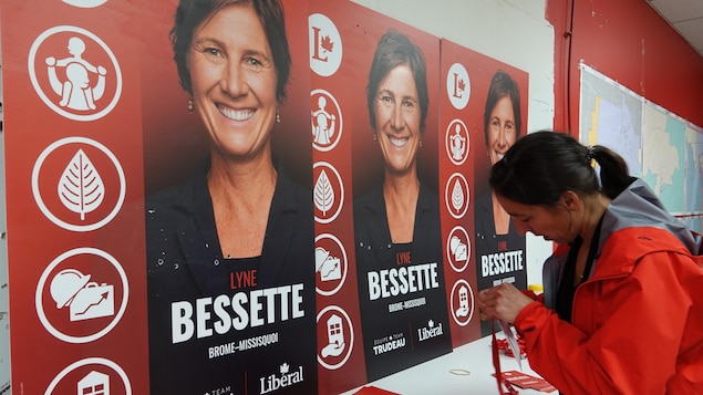 L'attachée assemble des cocardes devant des pancartes électorales de Lyne Bessette.