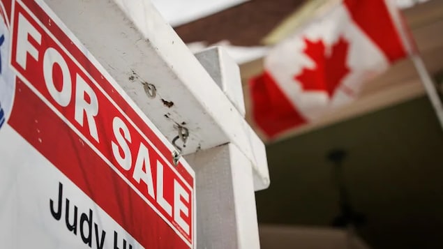 Un cartel de casa en venta con una bandera canadiense ondeando en el trasfondo.