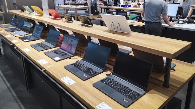Une vingtaine d'ordinateurs et de tablettes sont placées sur un meuble en bois, dans un magasin.
