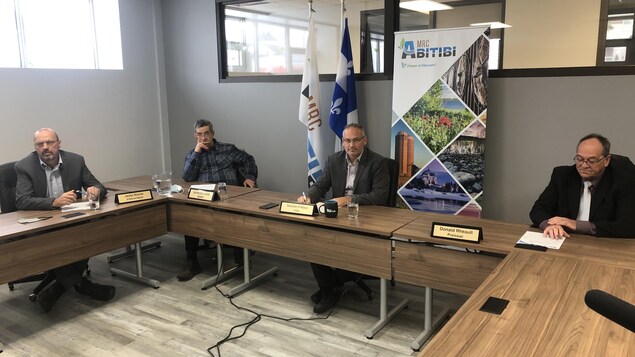 Les quatre hommes sont assis derrière des tables placées en U.