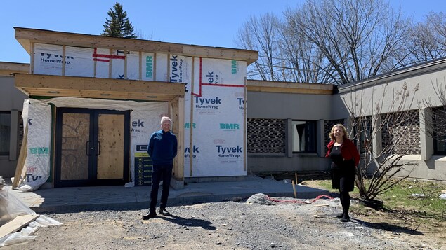 Deux personnes debout devant une bâtisse dont la construction n'est pas terminée.