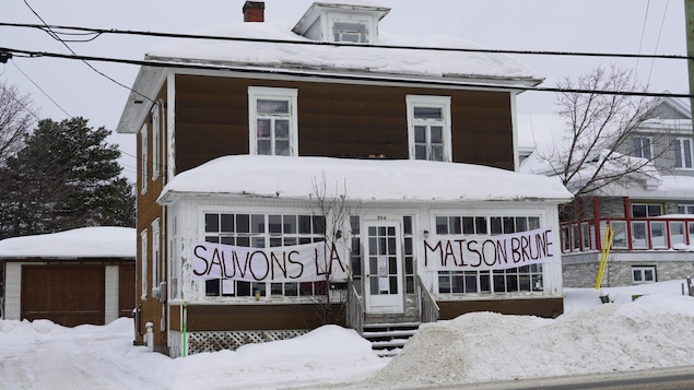 Une banderole sur laquelle les mots "Sauvons la maison brune" est accrochée sur la façade la maison en papier brique, en hiver.