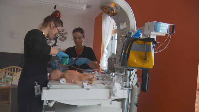 Deux femmes sont penchées au-dessus d'un nourrisson en plastique sur une table chaude. 