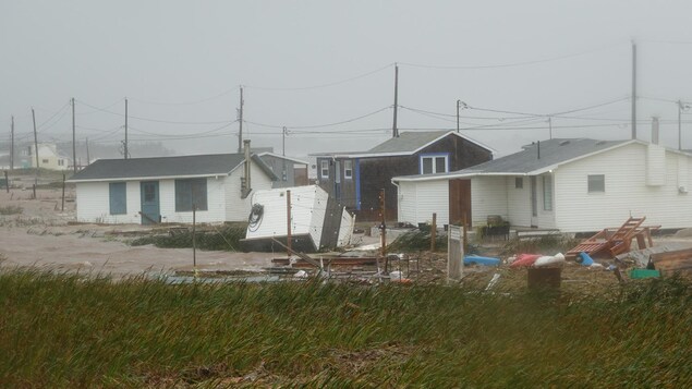 Des maisons inondées, avec une roulotte et des meubles éparpillés tout autour.