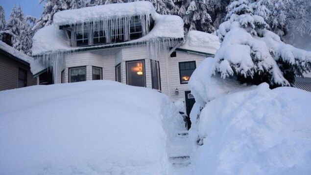 Une maison résidentielle en bois entourée d'une immense quantité de neige.