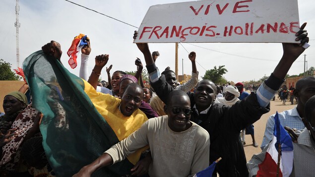 Des Maliens sourient et crient dans la rue. L'un d'eux tient une pancarte sur laquelle il est écrit : « Vive François Hollande ». Des Maliens sourient et crient dans la rue. L'un d'eux tient une pancarte sur laquelle il est écrit : « Vive François Hollande ».