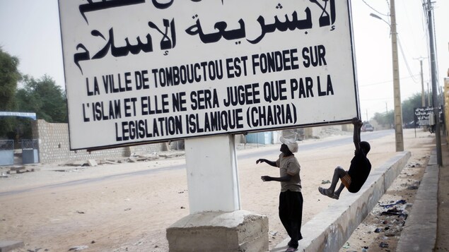 Deux jeunes Maliens se balancent sous une affiche blanche sur laquelle il est écrit en arabe et en français : « La ville de Tombouctou est fondée sur l'Islam et elle ne sera jugée que par la législation islamique (charia) ». Deux jeunes Maliens se balancent sous une affiche blanche sur laquelle il est écrit en arabe et en français : « La ville de Tombouctou est fondée sur l'Islam et elle ne sera jugée que par la législation islamique (charia) ».