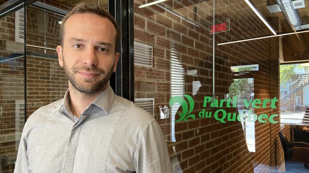 Un homme devant une porte en verre sur laquelle est écrit le Parti verte du Québec.