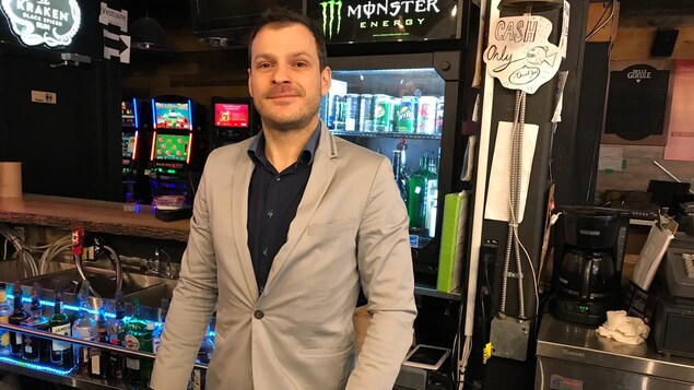 Mathieu Malouin, portant une chemise et un veston, derrière le bar de son établissement rue Sainte-Catherine et souriant devant la caméra. Mathieu Malouin, portant une chemise et un veston, derrière le bar de son établissement rue Sainte-Catherine et souriant devant la caméra.