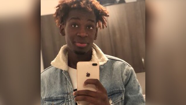 Photo de Mamadou Kailou Barry. Il tient un iphone de couleur blanche et. regarde un miroir. Il a la peau noire et des cheveux frisés teints roux.