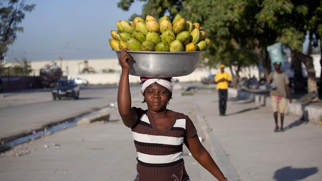 Une vendeuse transporte un grand bol métallique remplis de plusieurs dizaines de mangues sur sa tête. Elle vend 5 fruits pour 2 dollars dans les rues de Port-au-Prince.