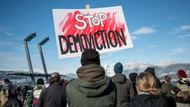 Un manifestant tient une pancarte lors d’un rassemblement pour les logements à Vancouver en février. Un manifestant tient une pancarte lors d’un rassemblement pour les logements à Vancouver en février.
