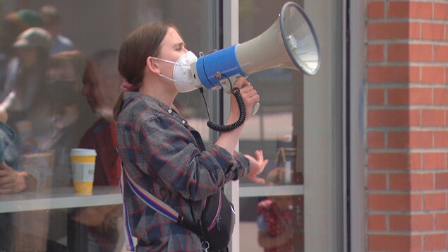Une manifestante s'adresse à la foule à travers un porte-voix devant un bâtiment.