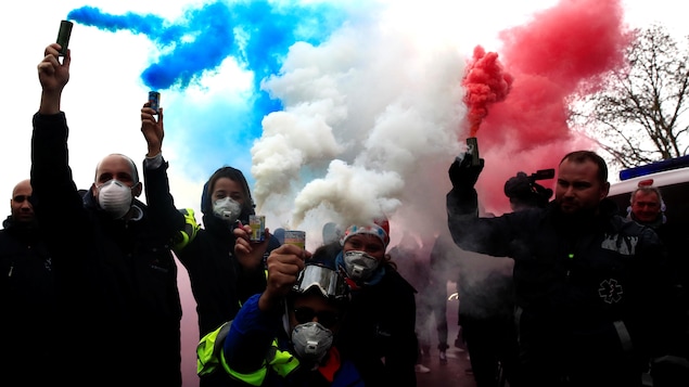 Des ambulanciers qui tiennent des fumigènes bleu, blanc rouge.