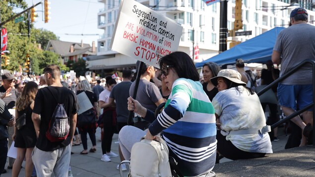 Una mujer se sienta en las escaleras en medio de una manifestación con una pancarta en la mano.