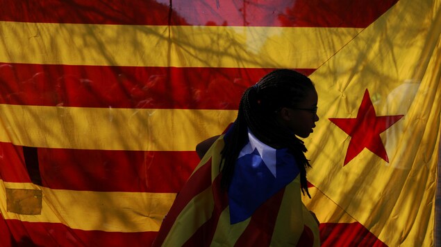 Une femme portant un drapeau indépendantiste catalan passe devant un autre drapeau coloré durant une manifestation à Barcelone.