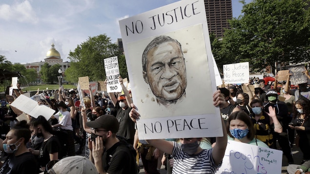 Au milieu d'une foule nombreuse, une jeune femme tient une pancarte sur laquelle on peut voir une illustration de George Floyd avec les mots « Pas de justice, pas de paix » lors d'une manifestation contre la brutalité policière à Boston.