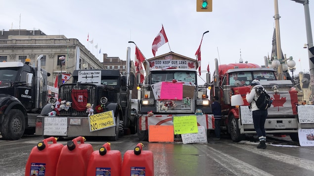 Cans of gasoline in front of trucks parked next to each other and covered with signs.