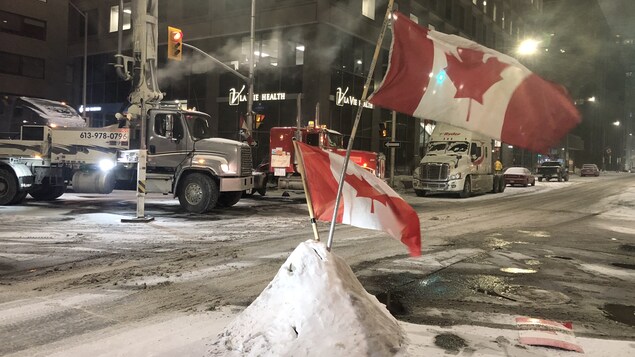 Des drapeaux du Canada plantés dans la neige au milieu de la rue.