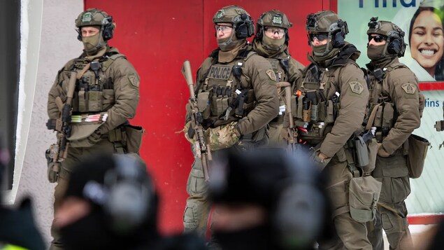 Des membres des forces de l'ordre en uniforme avec des armes en main se tiennent prêts à intervenir.