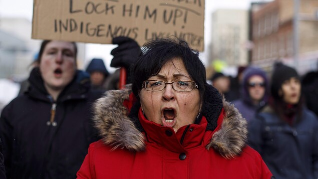 Une femme pleure lors d'une manifestation à Edmonton. Derrière elle, un homme tient une pancarte.