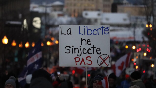 Une femme tient une pancarte sur laquelle on peut lire : La liberté ne s'injecte pas.