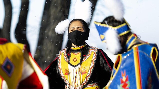 Des femmes portent leur costumes de cérémonies avec des perles et un masque sur leur visage.