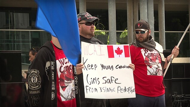 Trois membres de la WCAI tiennent des drapeaux et une affiche