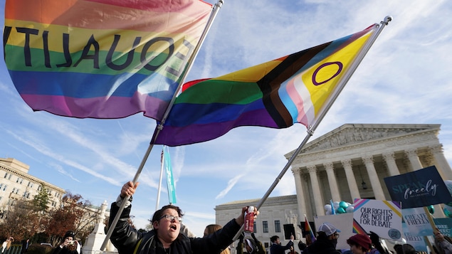 Une femme tient à bout de bras deux drapeaux aux couleurs de la communauté LGBT devant la Cour suprême.
