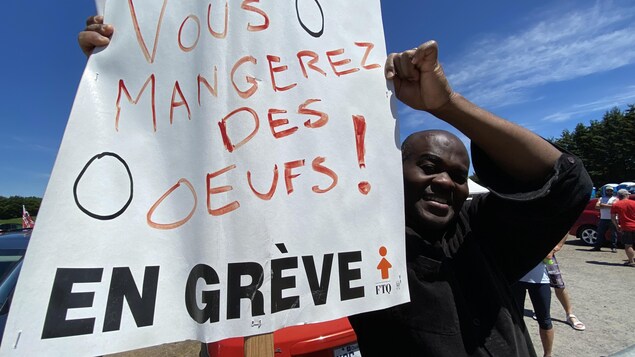 Un homme tient une pancarte sur laquelle on peut lire « Vous mangerez des oeufs »