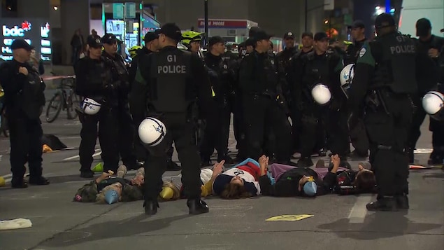 Des manifestants sont couchés au sol et entourés de policiers.