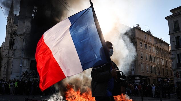 Un manifestant brandit un drapeau de la France devant un incendie de débris dans la rue.