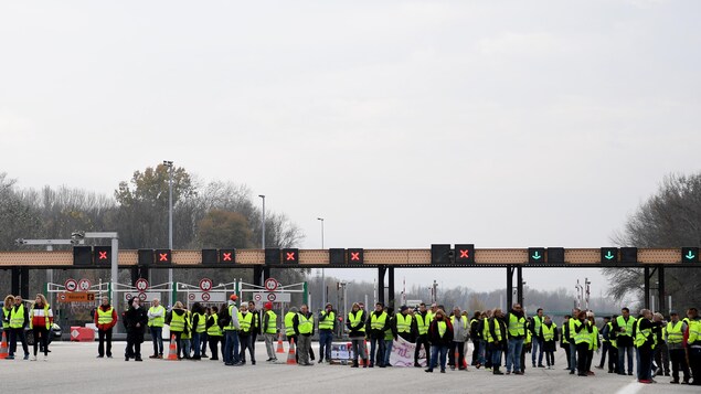 Plusieurs personnes vêtues d'un gilet jaune devant des barrières de péage. Plusieurs personnes vêtues d'un gilet jaune devant des barrières de péage.