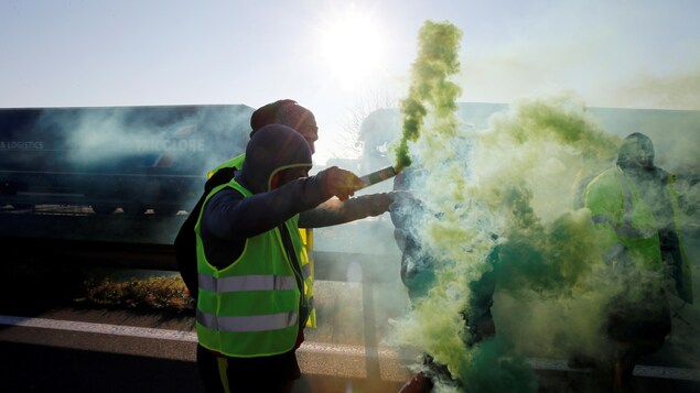 Des manifestants vêtus de gilets jaunes qui tiennent des fumigènes. Des manifestants vêtus de gilets jaunes qui tiennent des fumigènes.