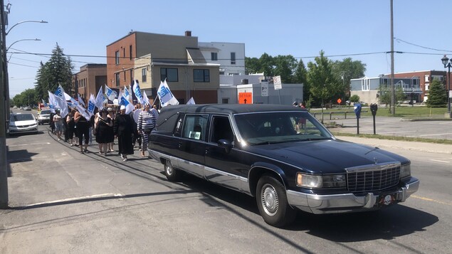 Un corbillard et des gens qui marchent avec des drapeaux.