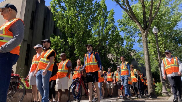 Prise de vue en contre-plongée d’ingénieurs défilant sur la Grande Allée vêtus de vestes orange. 