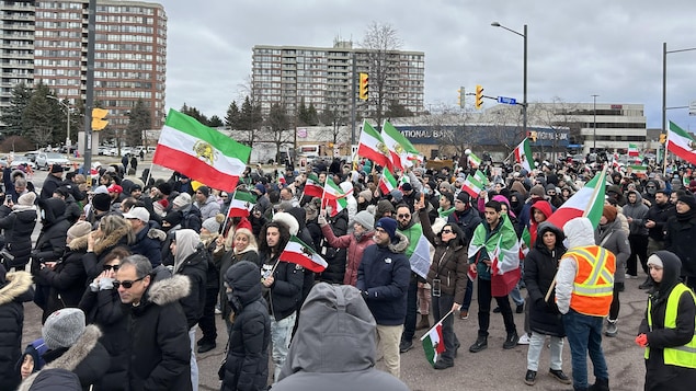 Des manifestants marchent dans les rues de Toronto et brandissent des drapeaux iraniens.