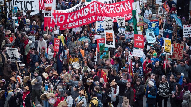 Des milliers de manifestants, certains en habits traditionnels autochtones, et plusieurs qui tiennent des pancartes sur lesquelles on peut lire an anglais Non Kinder Morgan, sont rassemblés.