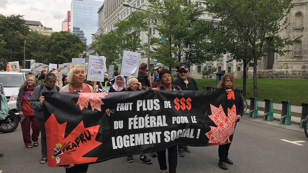Des manifestants tiennent une banderole sur laquelle on peut lire «Faut plus de dollars du fédéral pour le logement social».