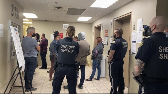 Des policiers et des résidents dans un couloir devant des ascenseurs.