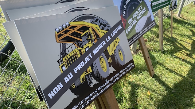 Des affiches qui comportent une image dessinée d'un camion transportant des roches. Au travers, une large bande sur laquelle il est écrit « Non au projet minier La Loutre ». Au bas de l'affiche, les noms de plusieurs municipalités et lacs.