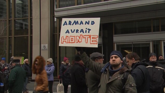 Un manifestant brandi une pancarte sur laquelle on peut lire : "Armand aurait honte." Un manifestant brandi une pancarte sur laquelle on peut lire : "Armand aurait honte."