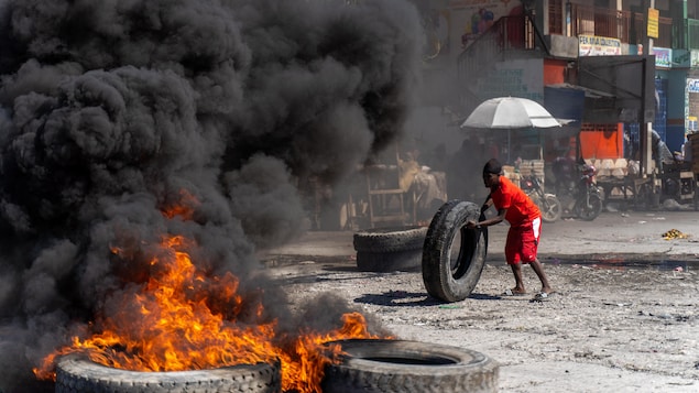 Un hombre lleva un neumático hacia las llamas. 